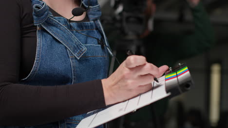 Female-Assistant-On-Film-Set-In-Studio-Writing-Movie-Or-Video-Production-Details-Down-On-Clapperboard-Or-Slate